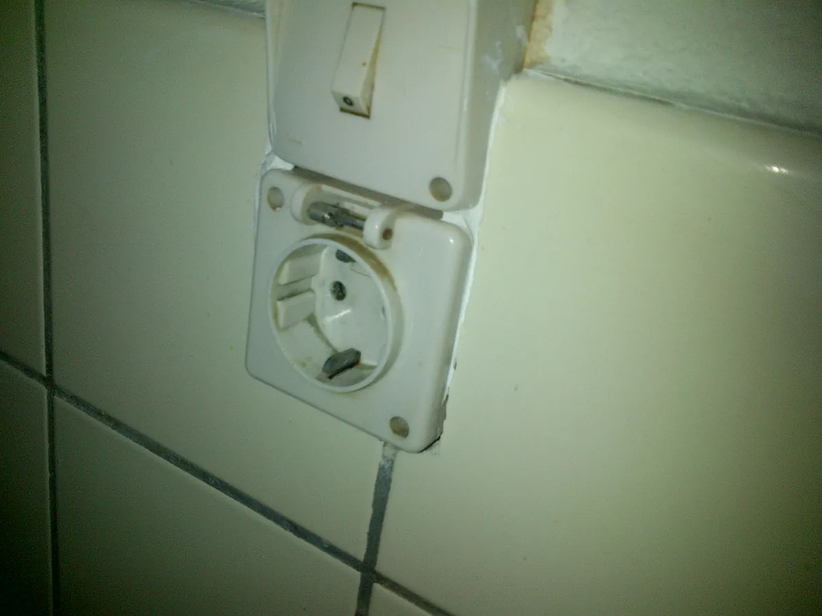 Stopcontact met randaarding en klapdeksel in een betegelde muur